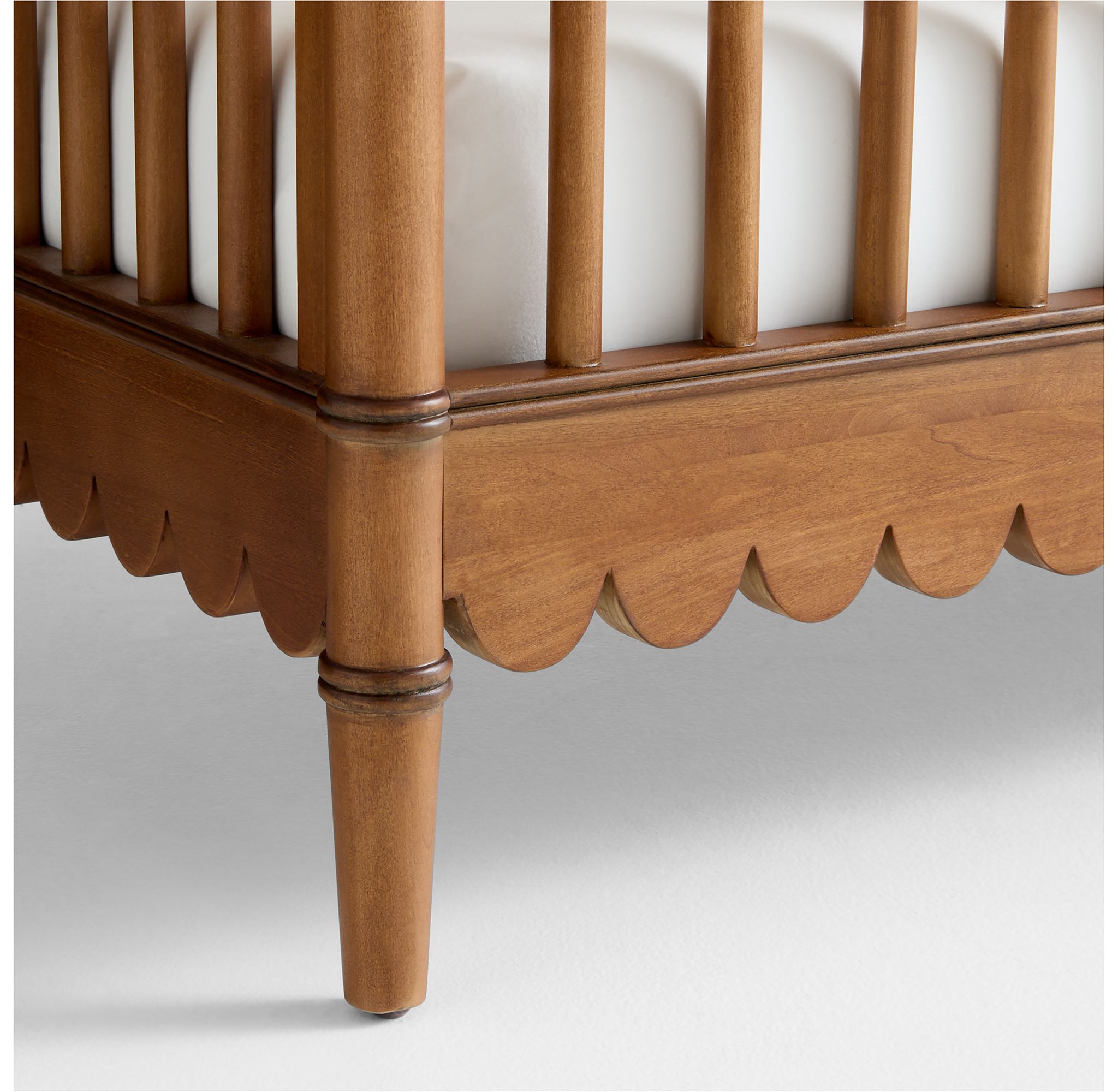 Close-up detail of the scalloped trim on the leg of an antique amber wood crib