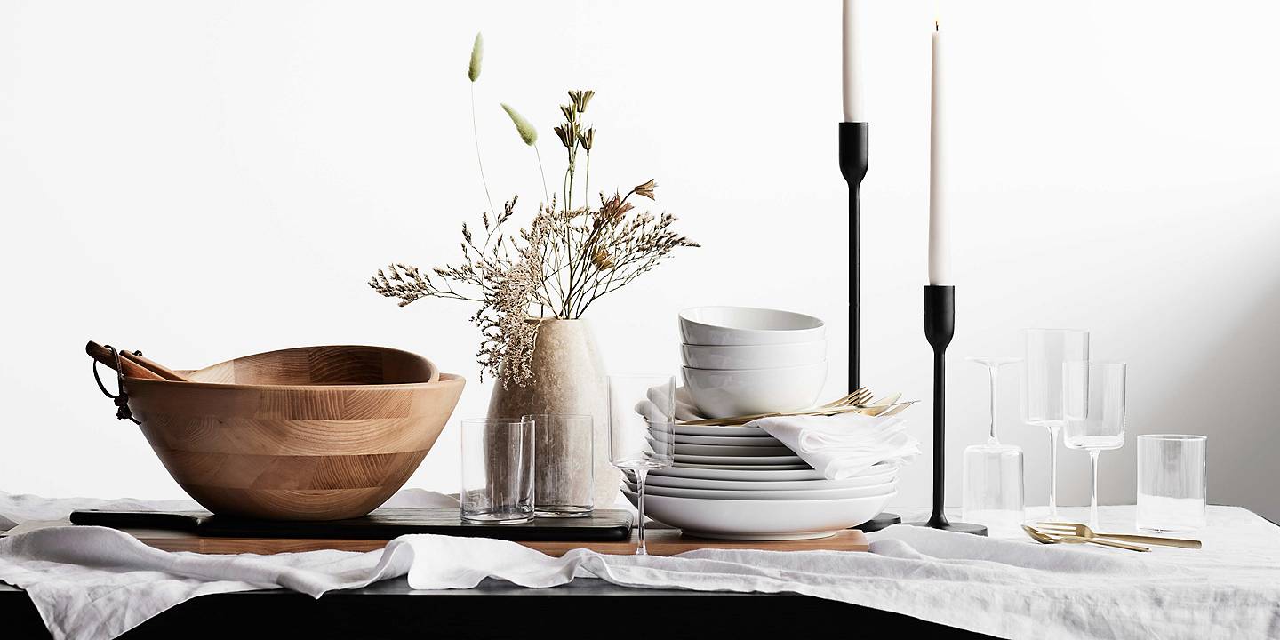 Close shot of faux botanicals in vase in the center of a dining table with serving and entertaining pieces
